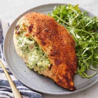 A plate with an air fryer stuffed chicken breast along with some arugula. A fork on the side with a napkin.