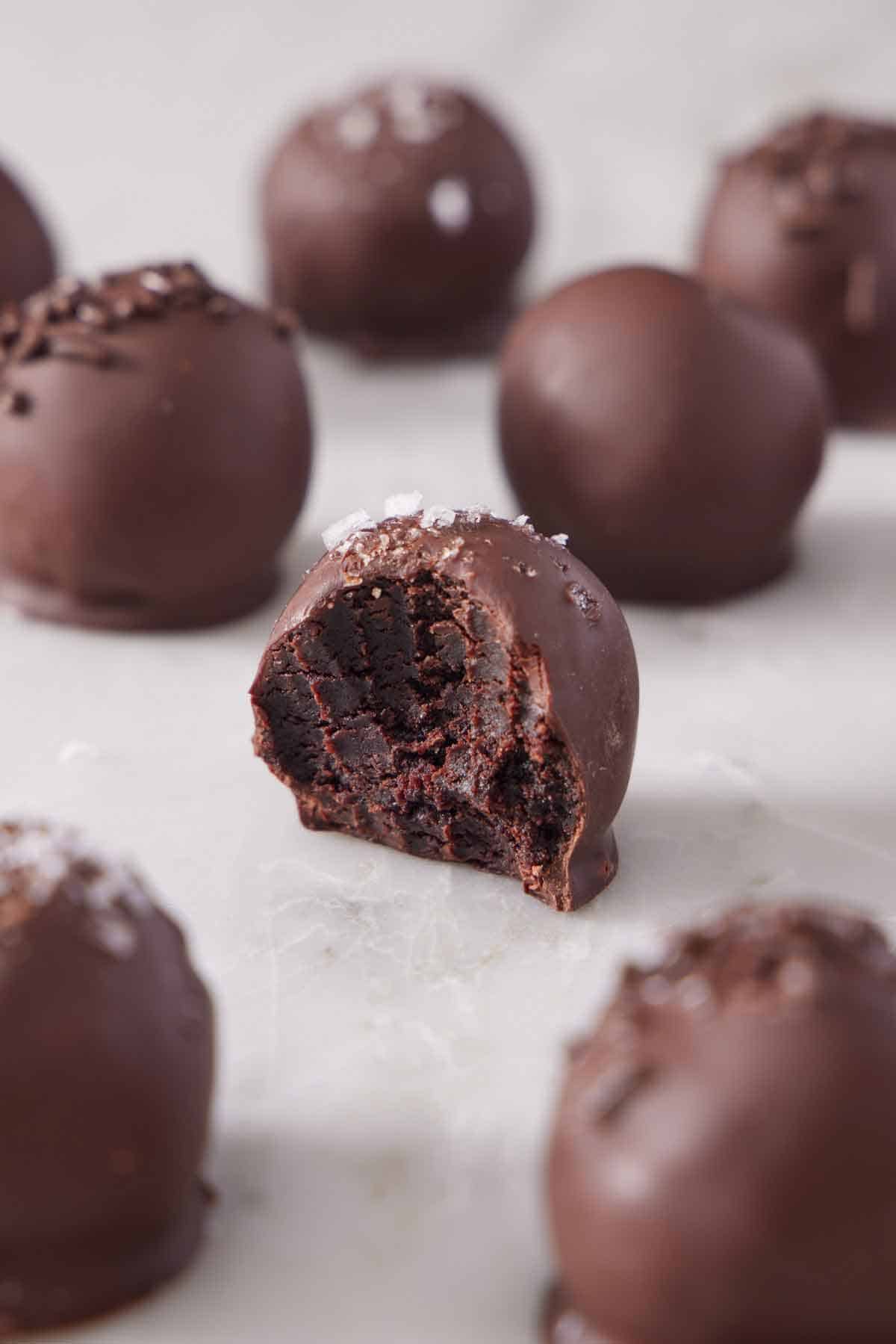 Brownie truffles in a single layer on a marble surface with the one in the middle with a bite taken out of it.