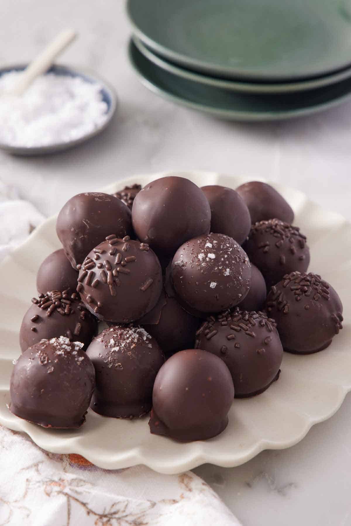 A scalloped platter of brownie truffles with a stack of plates and plate of salt in the background.