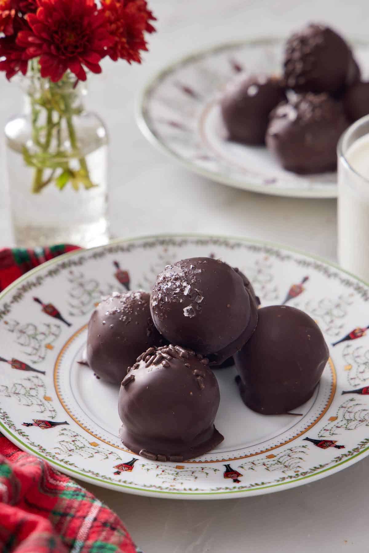 A plate of brownie truffles with one stacked on top. Flowers in the background along with another plate of brownie truffles.