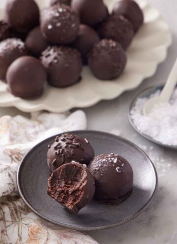 A plate with two and a half brownie truffles. A platter of more brownie truffles in the background along with a bowl of flaky salt.