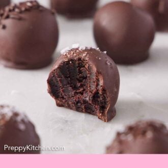 Pinterest graphic of brownie truffles in a single layer on a marble surface with the one in the middle with a bite taken out of it.