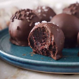 A plate of brownie truffles with the one in front with a bite taken out.