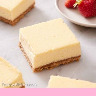 Pinterest graphic of cheesecake bars on a marble surface with a bowl of strawberries in the background.