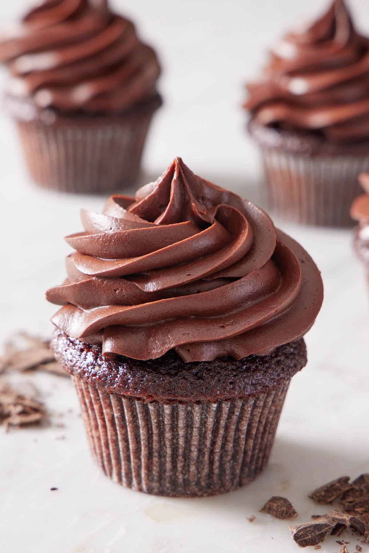 A chocolate cupcake with chocolate cream cheese frosting on top. More cupcakes in the background.