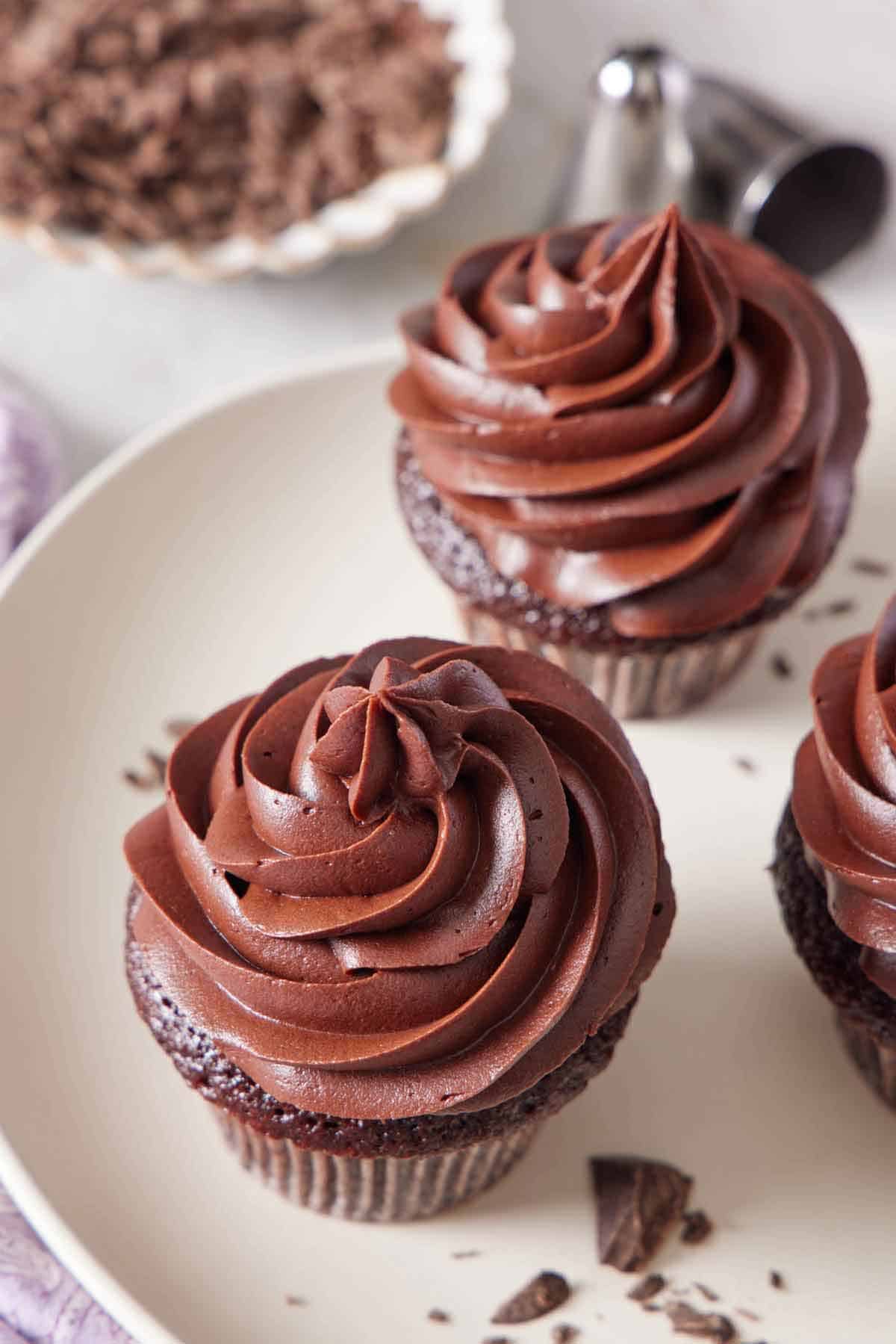 Chocolate cream cheese frosting piped over chocolate cupcakes on a plate.