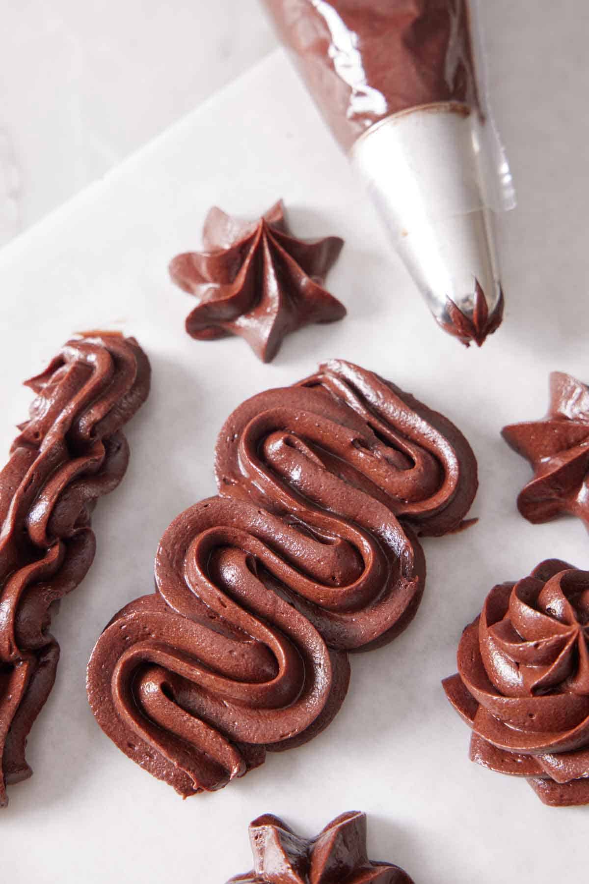 Chocolate cream cheese frosting pipped in different styles on a sheet of parchment paper.