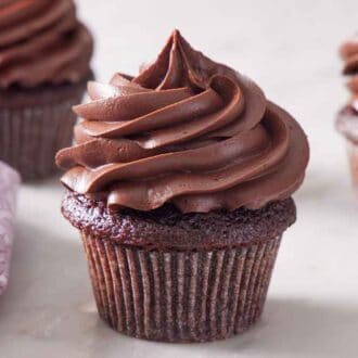 Three cupcakes topped with chocolate cream cheese frosting with one front and center.