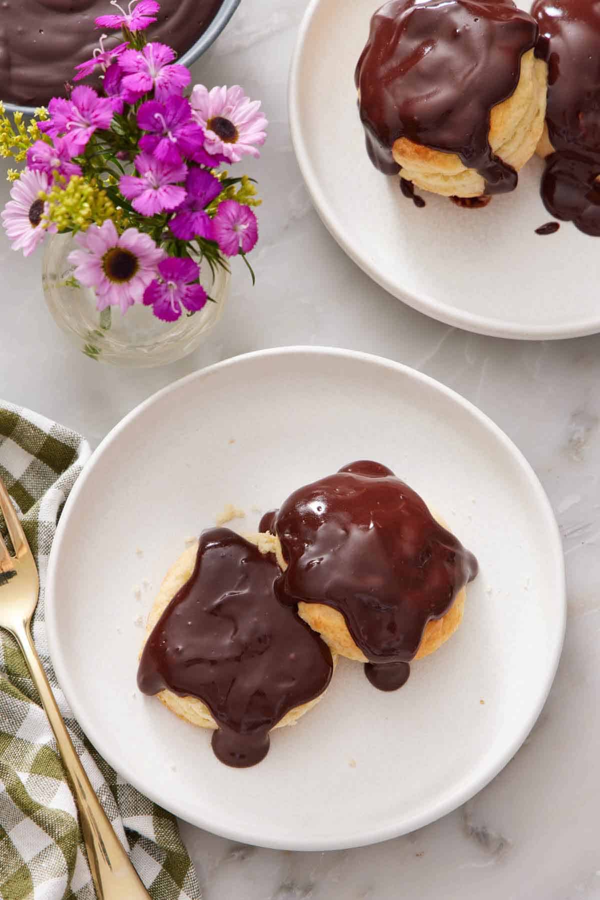 Overhead view of a plate of chocolate gravy over two biscuits. Another plate of biscuits with chocolate gravy and a vase of flower off to the side.