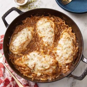 Overhead view of a skillet of French onion chicken. A linen napkin, fork, and some thyme off to the side.