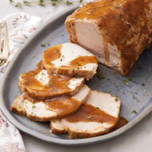 A platter of Instant Pot pork loin garnished with fresh thyme. A fork on the side.