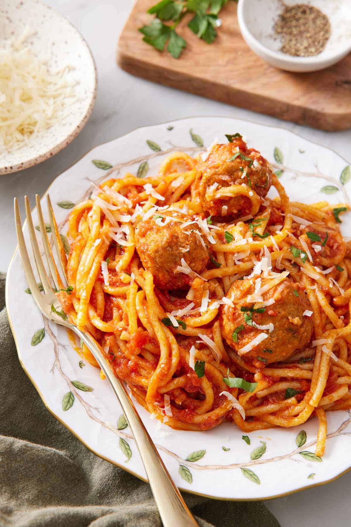 A plate of Instant Pot spaghetti and meatballs with a fork topped with parmesan and parsley. A bowl of pepper and parmesan in the back.