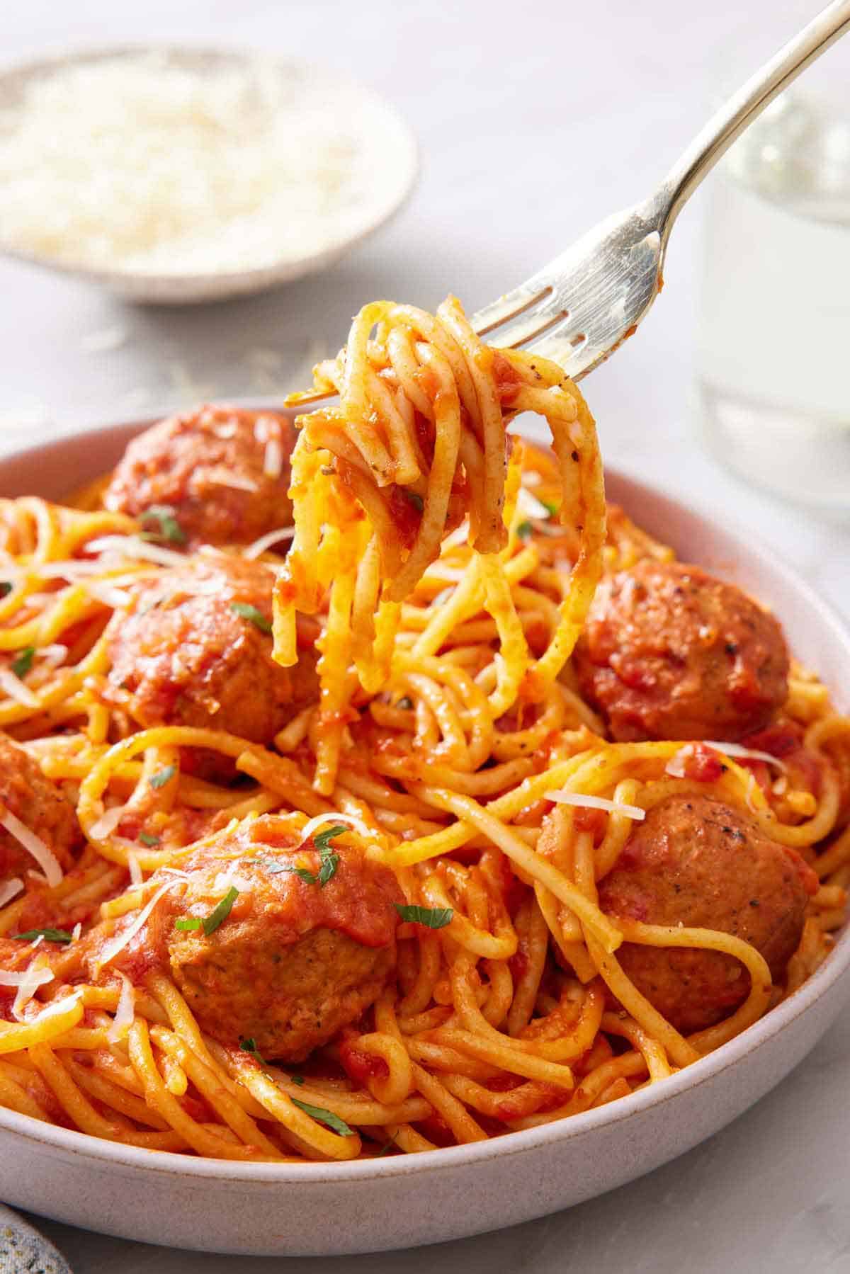 A fork lifting up a bite of Instant Pot spaghetti and meatballs from a plate.