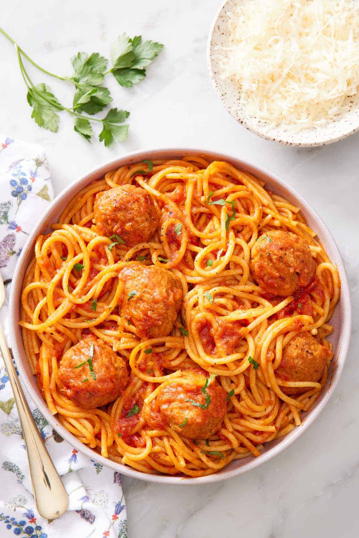 Overhead view of a plate of Instant Pot spaghetti and meatballs with chopped parsley on top. A bowl of parmesan on the side with more parsley.