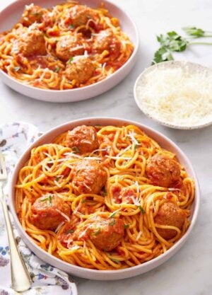 A plate of Instant Pot spaghetti and meatballs topped with parsley and parmesan. A bowl of parmesan and another plated serving of spaghetti and meatballs in the background.