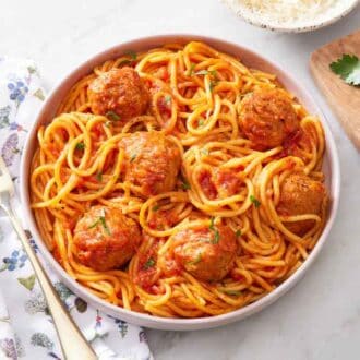 A plate of Instant Pot spaghetti and meatballs. Parsley, pepper, and a fork on the side.