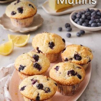 Pinterest graphic of a platter of lemon blueberry muffins. A bowl of blueberries, butter, lemon wedges, and a mini plate with another muffin on it in the background.