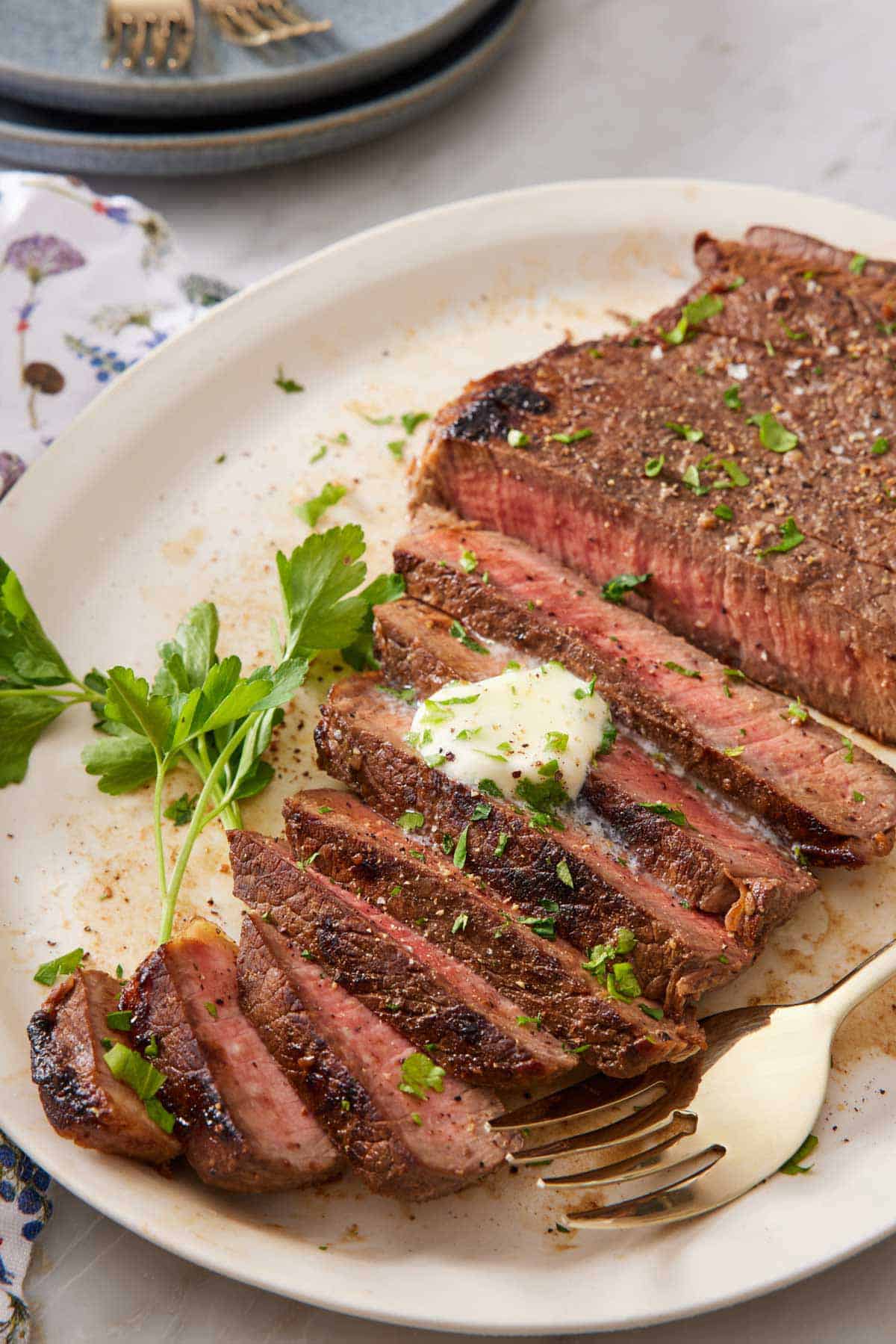 A platter with a London broil, partially sliced with a pat of melted butter on top and chopped herbs.