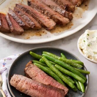 Pinterest graphic of a plate with two slices of London broil with green beans. A platter in the background with the rest of the sliced London broil.