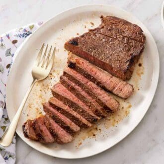 A platter with a partially sliced London broil with a fork. A bowl of green beans off to the side.