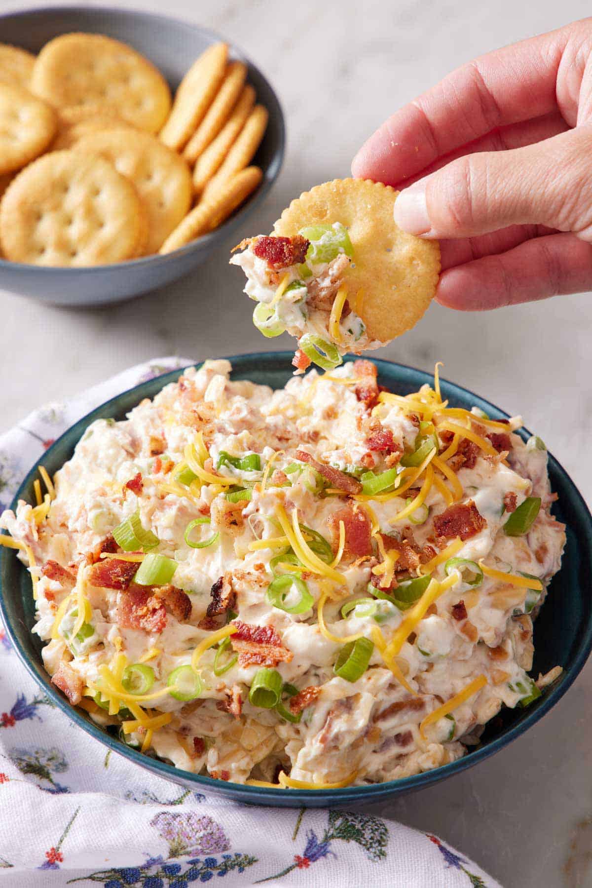 A bowl of million dollar dip with a cracker lifting up from the bowl after scooping some dip. More crackers in the bowl in the background.