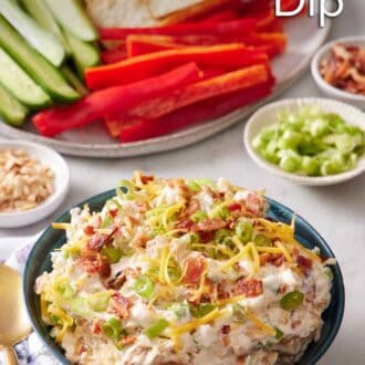 Pinterest graphic of a bowl of million dollar dip with a platter in the background with cucumbers, peppers, and crackers.