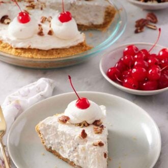 Pinterest graphic of a plate with a slice of Millionaire Pie with a dollop of whipped cream with a maraschino cherry on top. A bowl of maraschino cherries in the back along with the rest of the pie.