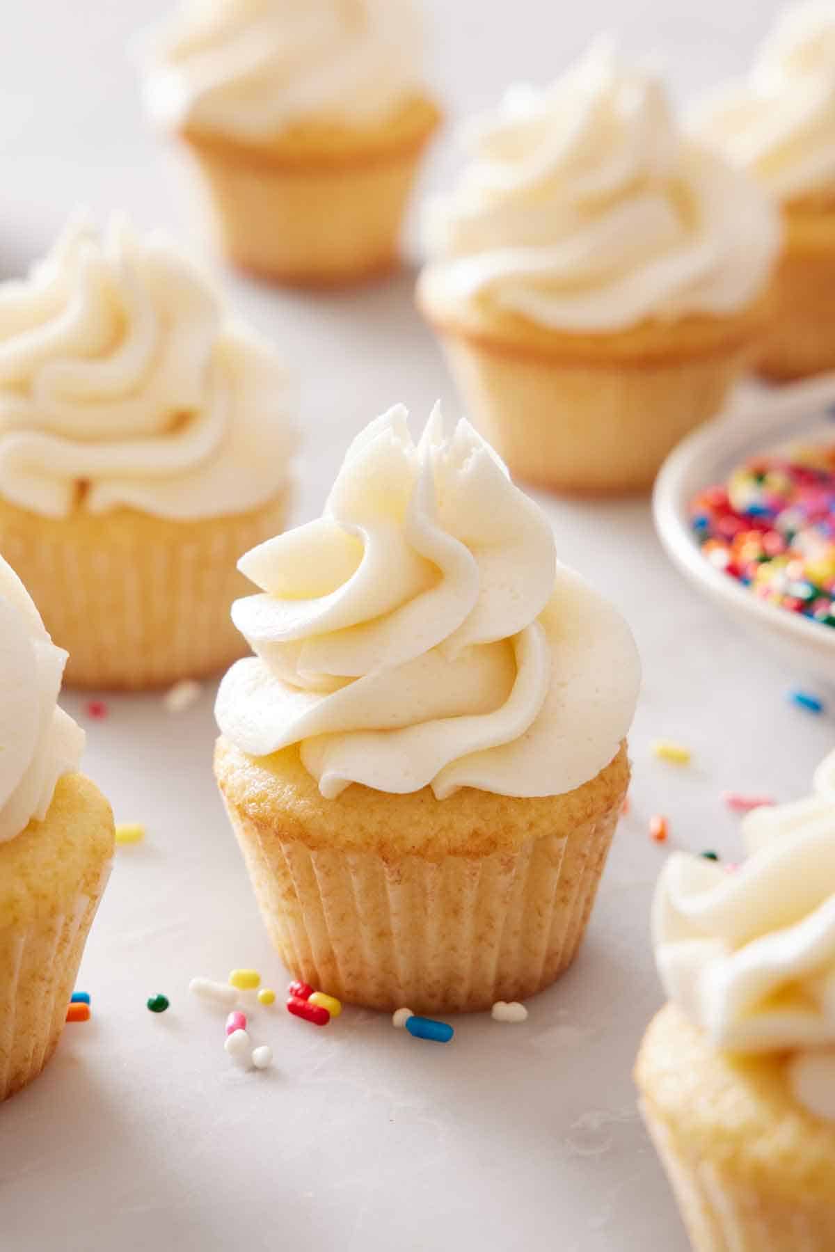 Multiple mini cupcakes with sprinkles scattered around on the marble surface.