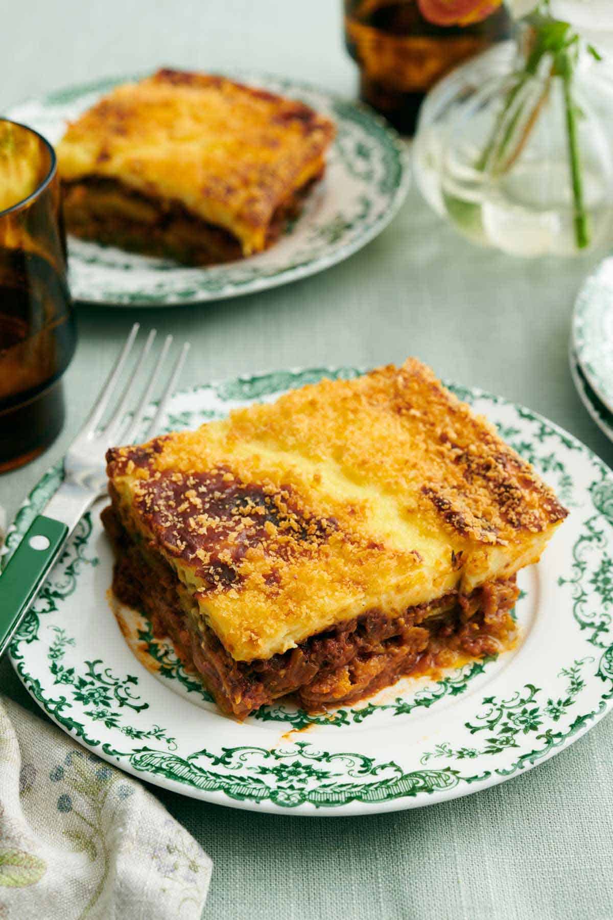 A plate of moussaka with a fork. Another plated serving in the background.