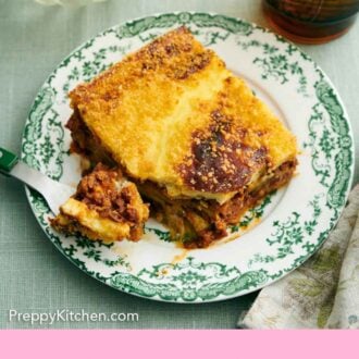 Pinterest graphic of a plate with a serving of moussaka with a bite on a fork.