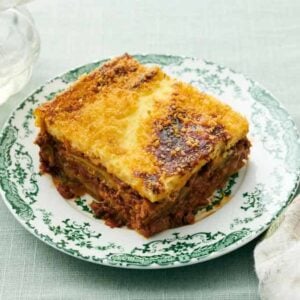 A plate with a serving of moussaka with a napkin on the side.