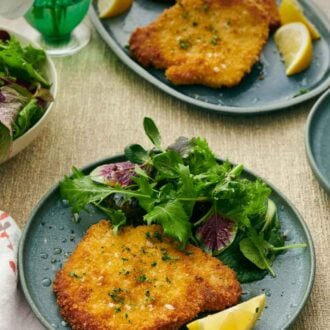 Pinterest graphic of a plate with a crispy schnitzel, mixed greens, and lemon wedge. A platter with more pork schnitzels in the background.