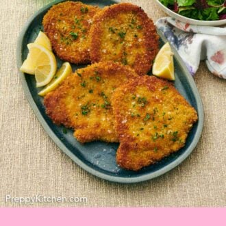 Pinterest graphic of a platter of schnitzels garnished with salt and parsley along with lemon wedges.