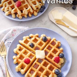 Pinterest graphic of a purple plate with a sourdough waffle topped with syrup, butter, and berries. Another plate of waffles and berries in the back along with a bowl of berries and butter.