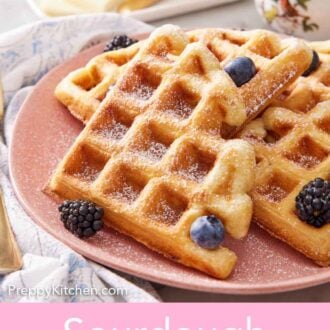 Pinterest graphic of a close up view of a plate with cut sourdough waffles topped with powdered sugar and berries.