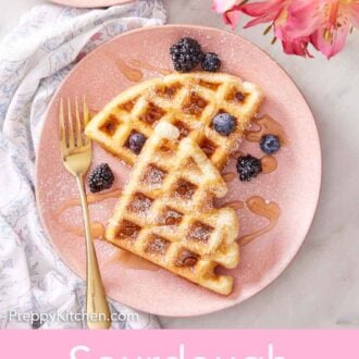 Pinterest graphic of an overhead view of sourdough waffles on a pink plate topped with maple syrup, powdered sugar, and berries with a fork.