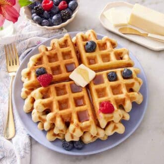 Overhead view of a stack of sourdough waffles with butter and berries on top and off to the side.