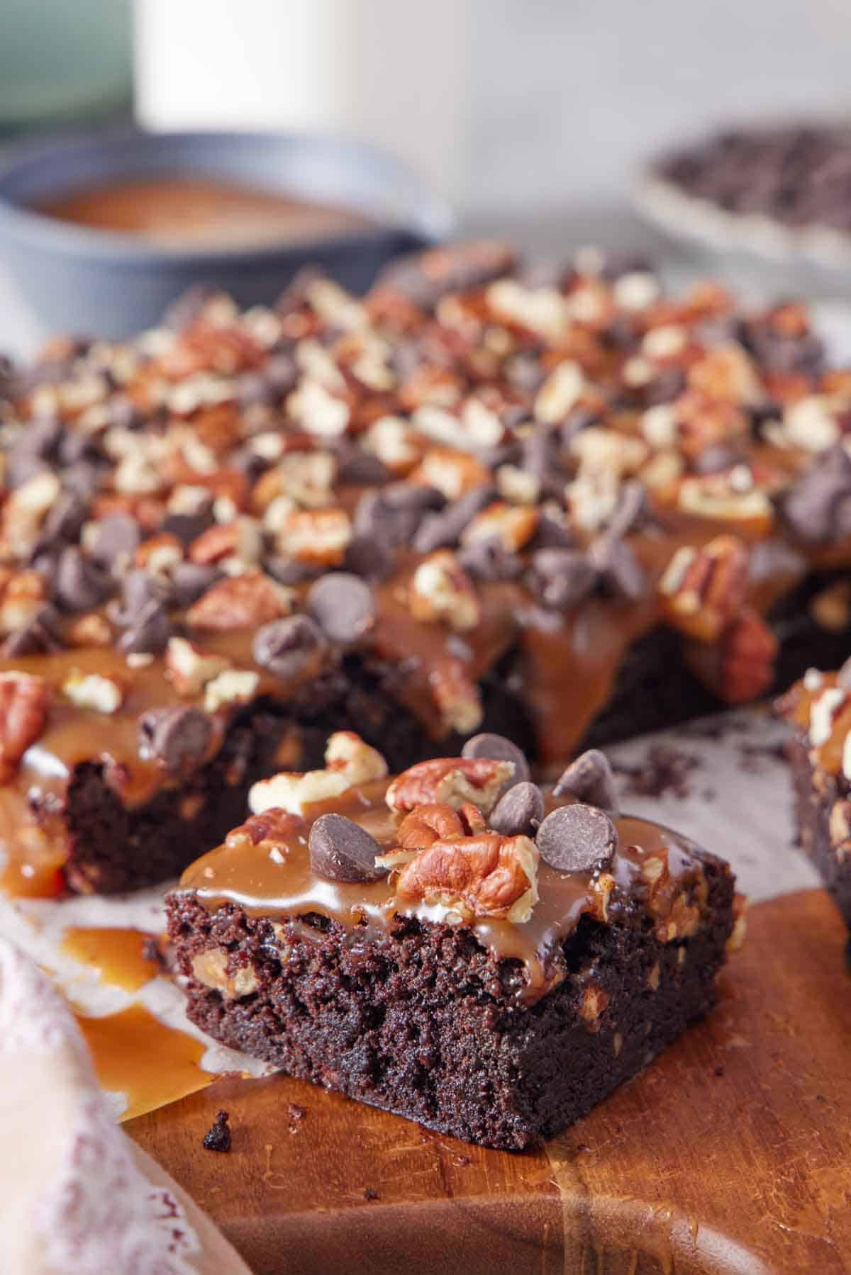 A serving board with turtle brownies with one piece cut out and pulled forward.