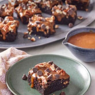 Pinterest graphic of a plate with a piece of turtle brownies with a platter more in the background along with a bowl of caramel.