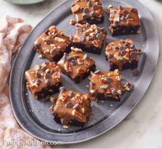 Pinterest graphic of a platter of turtle brownies with two plated servings in the back along with a plate of pecans and bowl of caramel sauce.