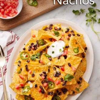 Pinterest graphic of a platter of air fryer nachos with chopped tomatoes, jalapenos, cilantro, black beans, and sour cream. More toppings in bowls on the side.