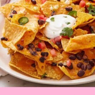 Pinterest graphic of a close up view of air fryer nachos on a platter, topped with sour cream, black beans, tomatoes, jalapeno, and cilantro.