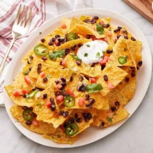 A platter of air fryer nachos with cilantro, green onions, sour cream, black beans, and jalapeno.
