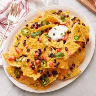 A platter of air fryer nachos with cilantro, green onions, sour cream, black beans, and jalapeno.