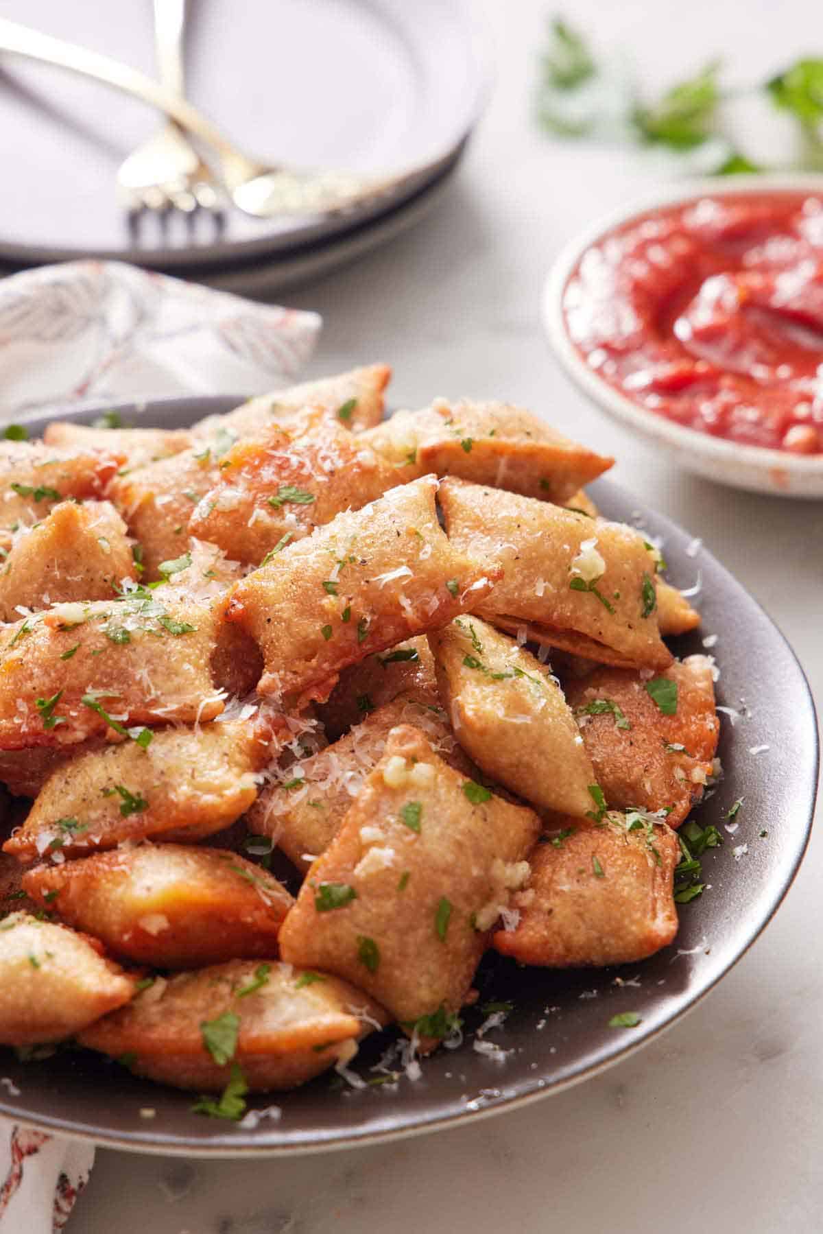 A close up view of air fryer pizza rolls with chopped parsley and parmesan on top. A bowl of marinara sauce in the background.