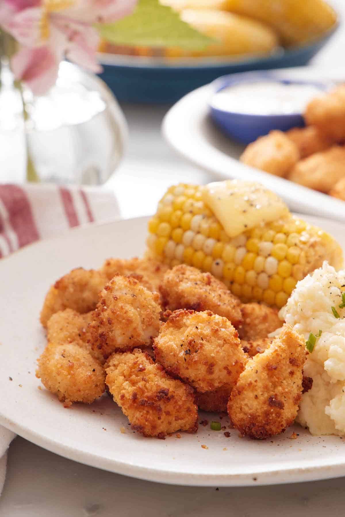 A close up view of air fryer popcorn chicken on a plate with mashed potatoes and a corn on the cob with butter.