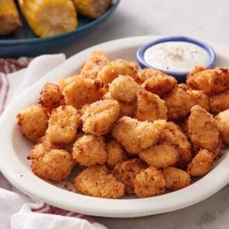 A platter of air fryer popcorn chicken with a small bowl of dipping sauce. A plate of corn in the background.