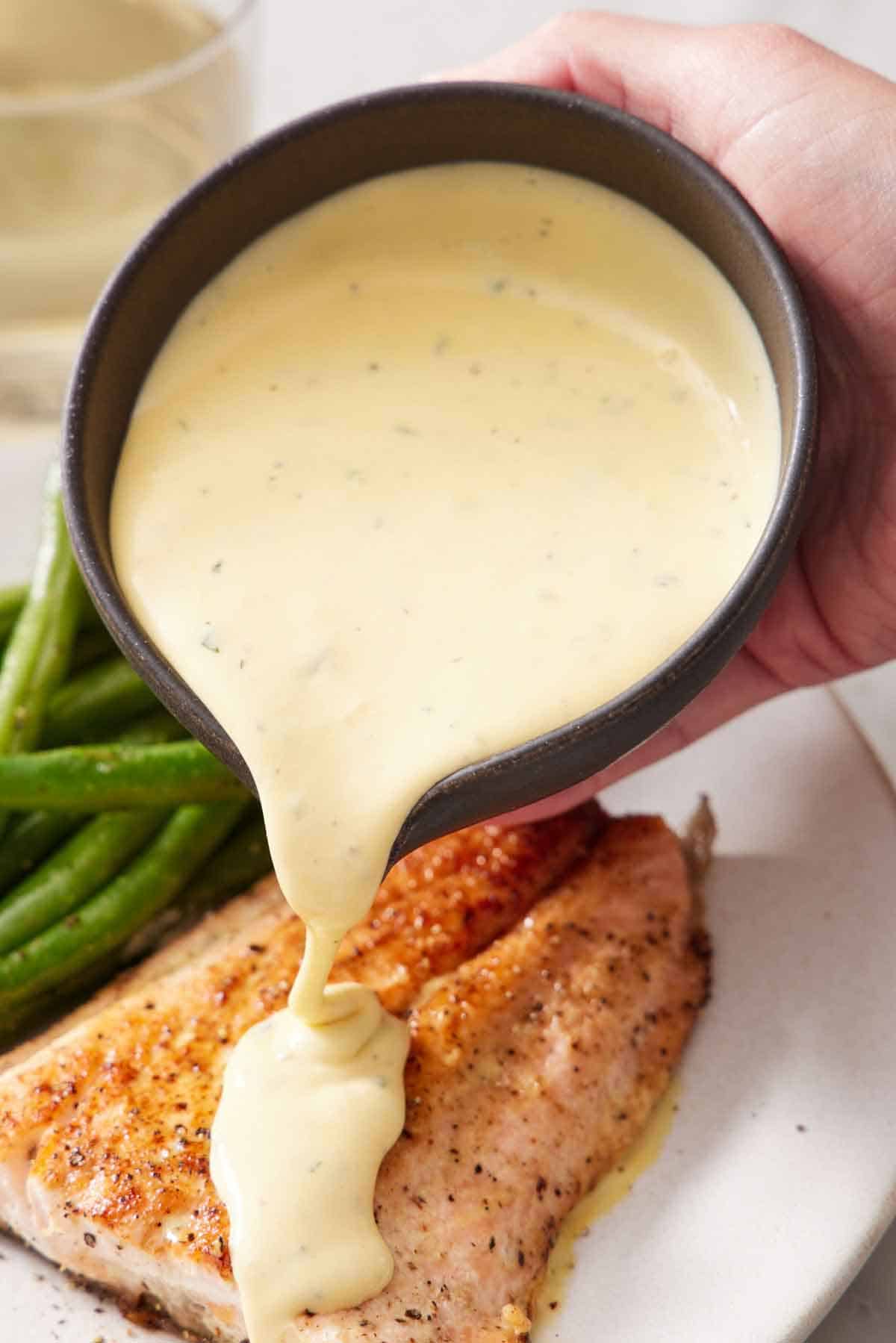 A bowl of béarnaise sauce poured over salmon on a plate.