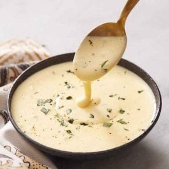 Béarnaise sauce in a spoon lifted from a bowl. Chopped tarragon as garnish over the sauce.