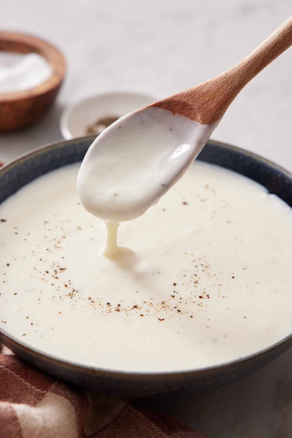 A spoon lifting up some béchamel sauce from a bowl.